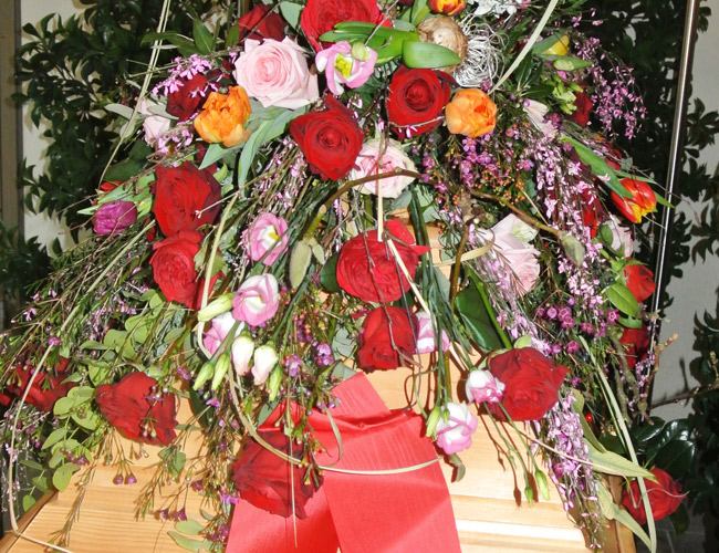Holzsarg mit rotem Band und Blumen
